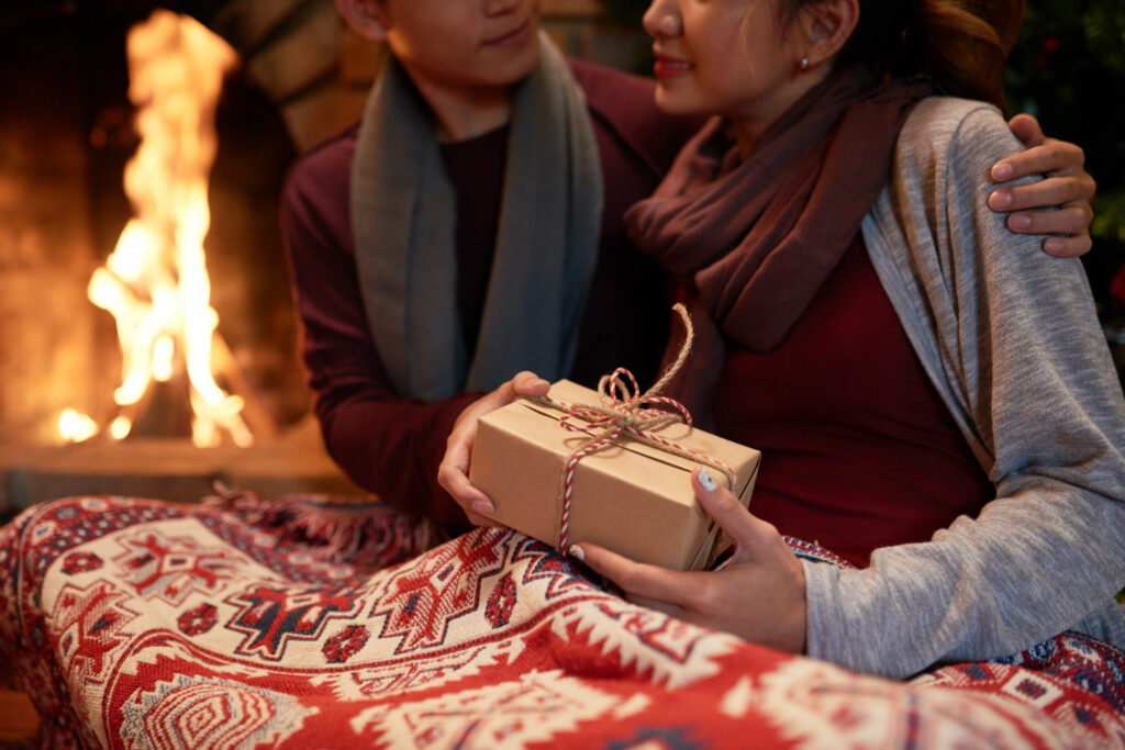 closeup of young couple cuddling at the fireplace with a present in female hands