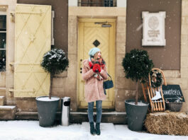 lady in pink coat stands before wooden doors in snowy weather