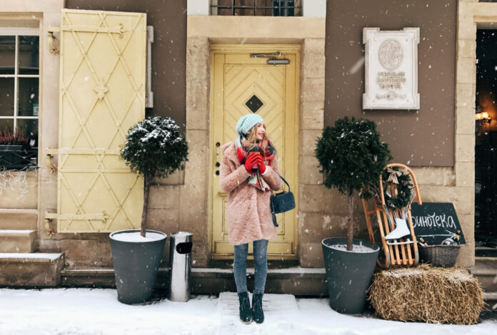 lady in pink coat stands before wooden doors in snowy weather