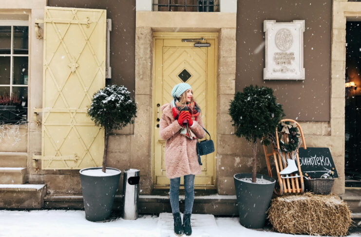 lady in pink coat stands before wooden doors in snowy weather