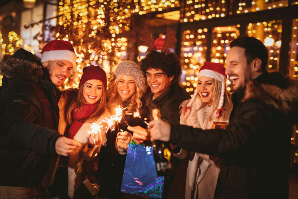 three couple with sparklers enjoying christmas outdoor party in the city street at night and with a lot of lights on