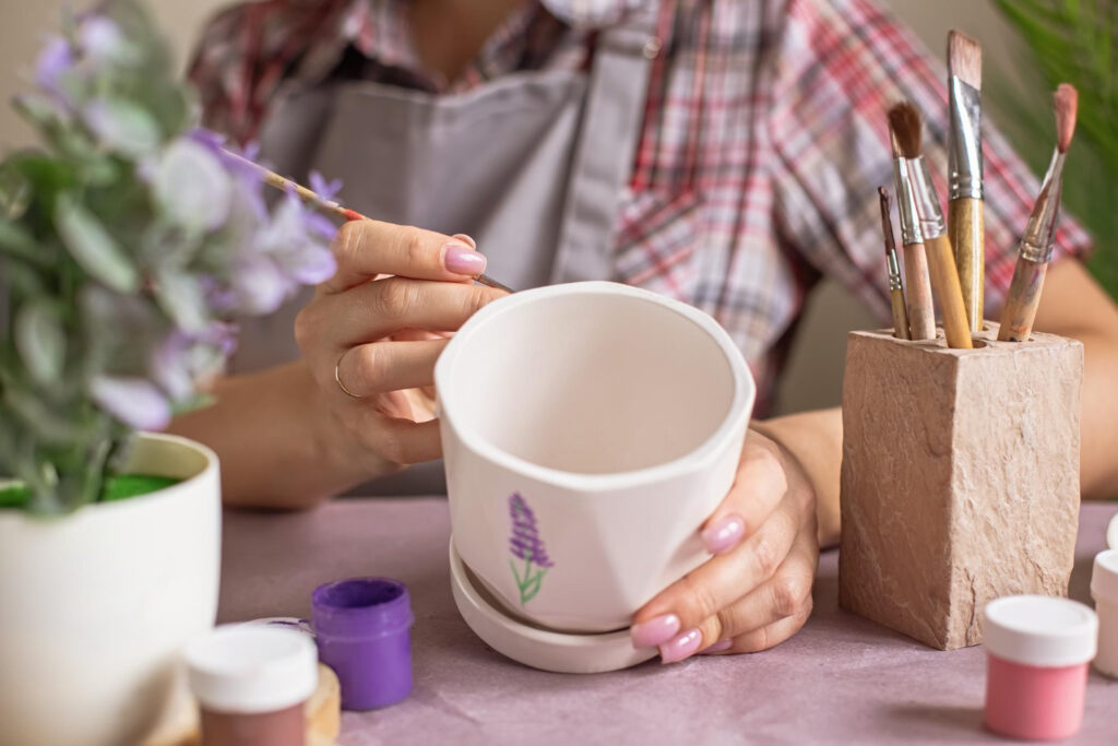 women in gray apron paint a white flower ceramic pot