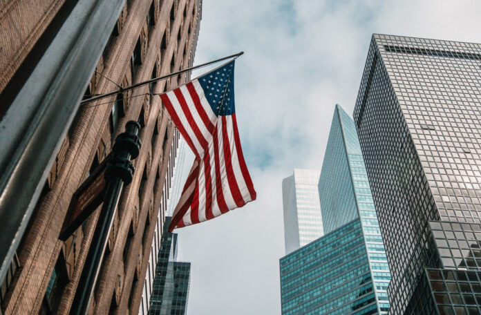 the usa or united states of america flag on a flagpole near skyscrapers under a cloudy sky