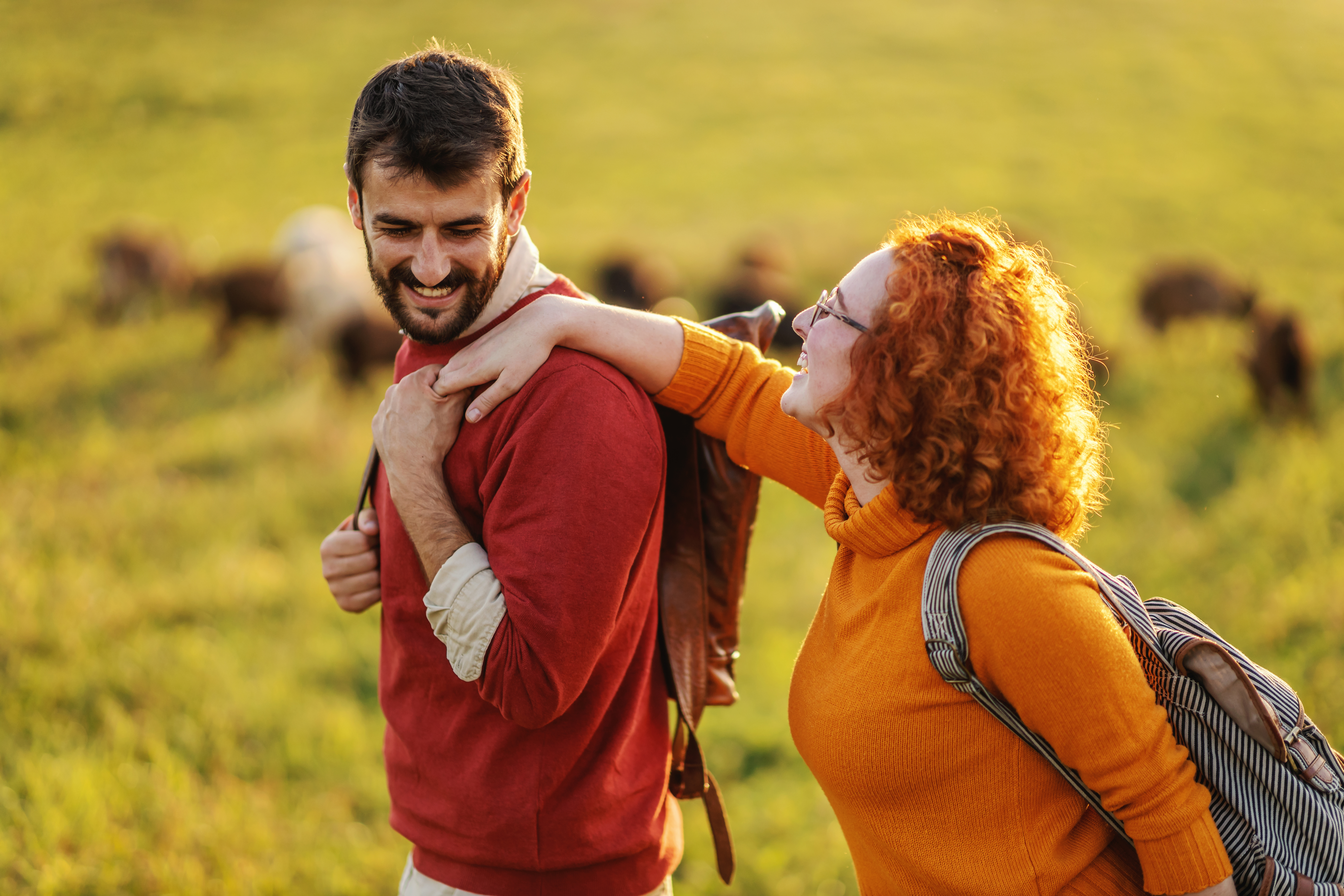 Couple spending free time in nature on a beautiful sunny autumn day. Couple holding hands and walking. In background, on a meadow, are goats.